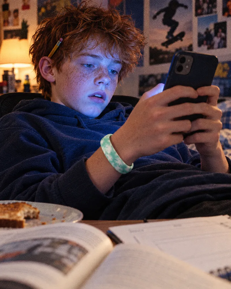 A boy at his desk, homework open and forgotten, hooked on his phone, a mint Sky Loop on his wrist