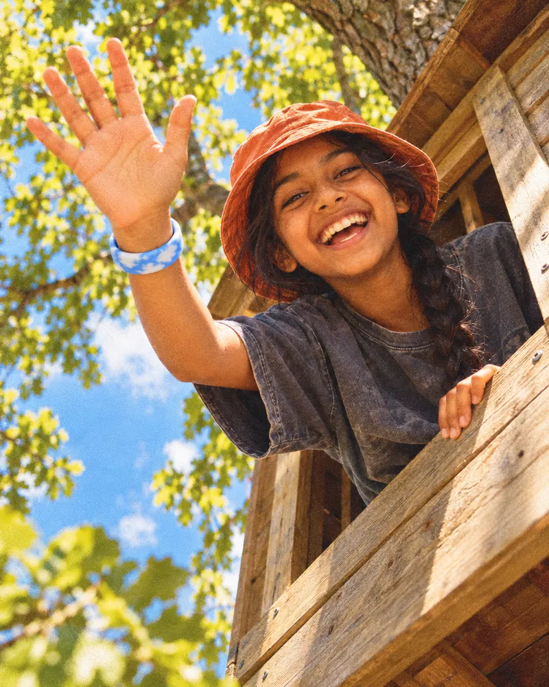 A girl waving out of a treehouse window, a cobalt Sky Loop on her waving wrist