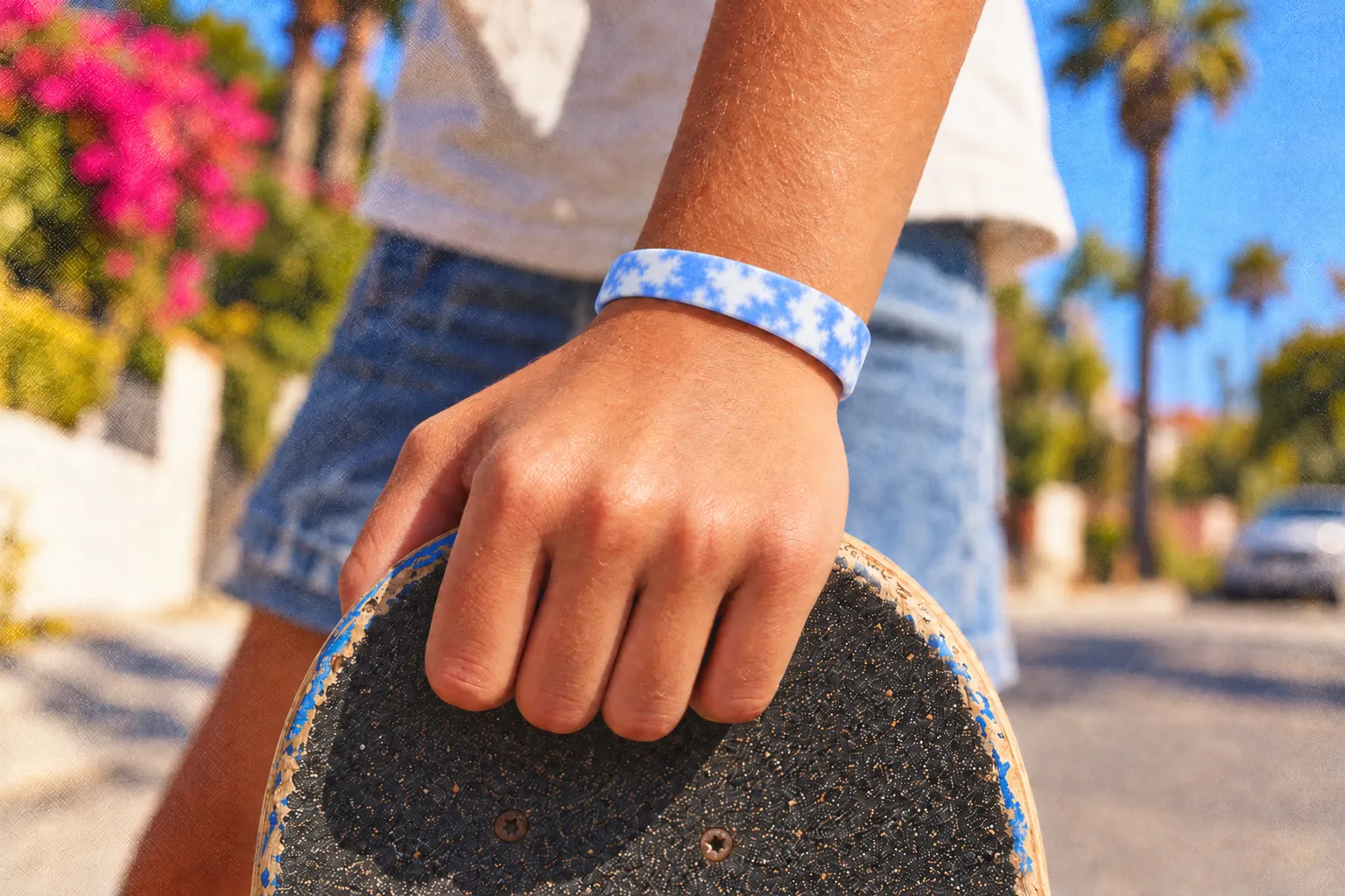 A kid’s hand gripping a skateboard on a sunny street, a cobalt Sky Loop on the wrist